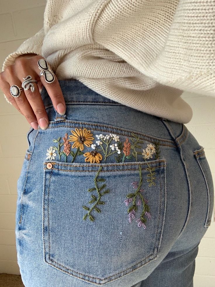 a woman with her back to the camera, wearing jeans with embroidered flowers on them
