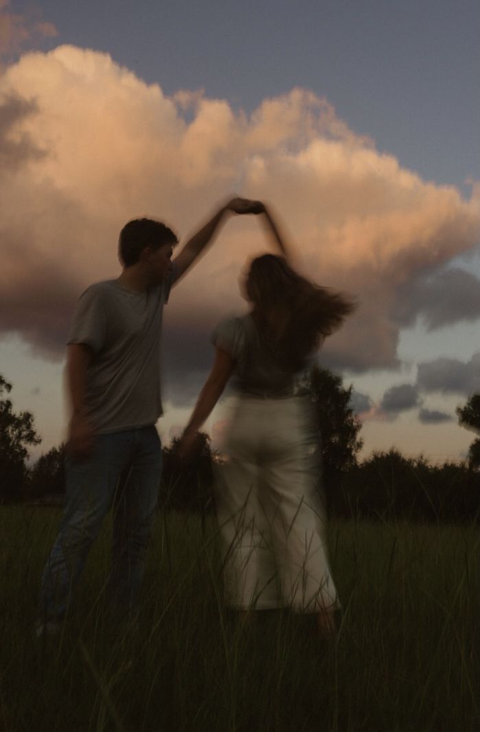 two people standing in the grass with their arms around each other and one person reaching for something