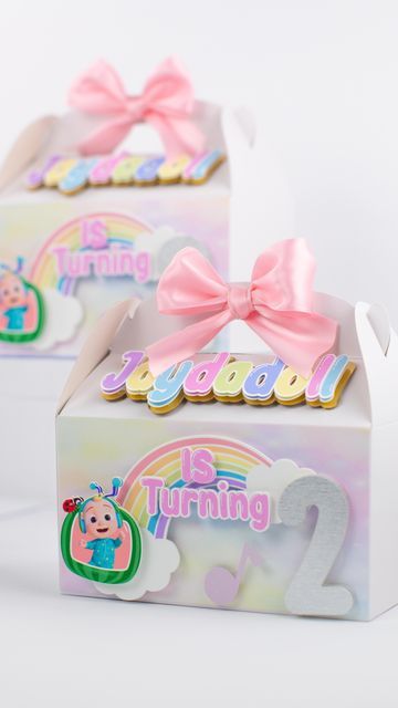 two boxes with pink bows on the top and one box has an image of a baby's first birthday