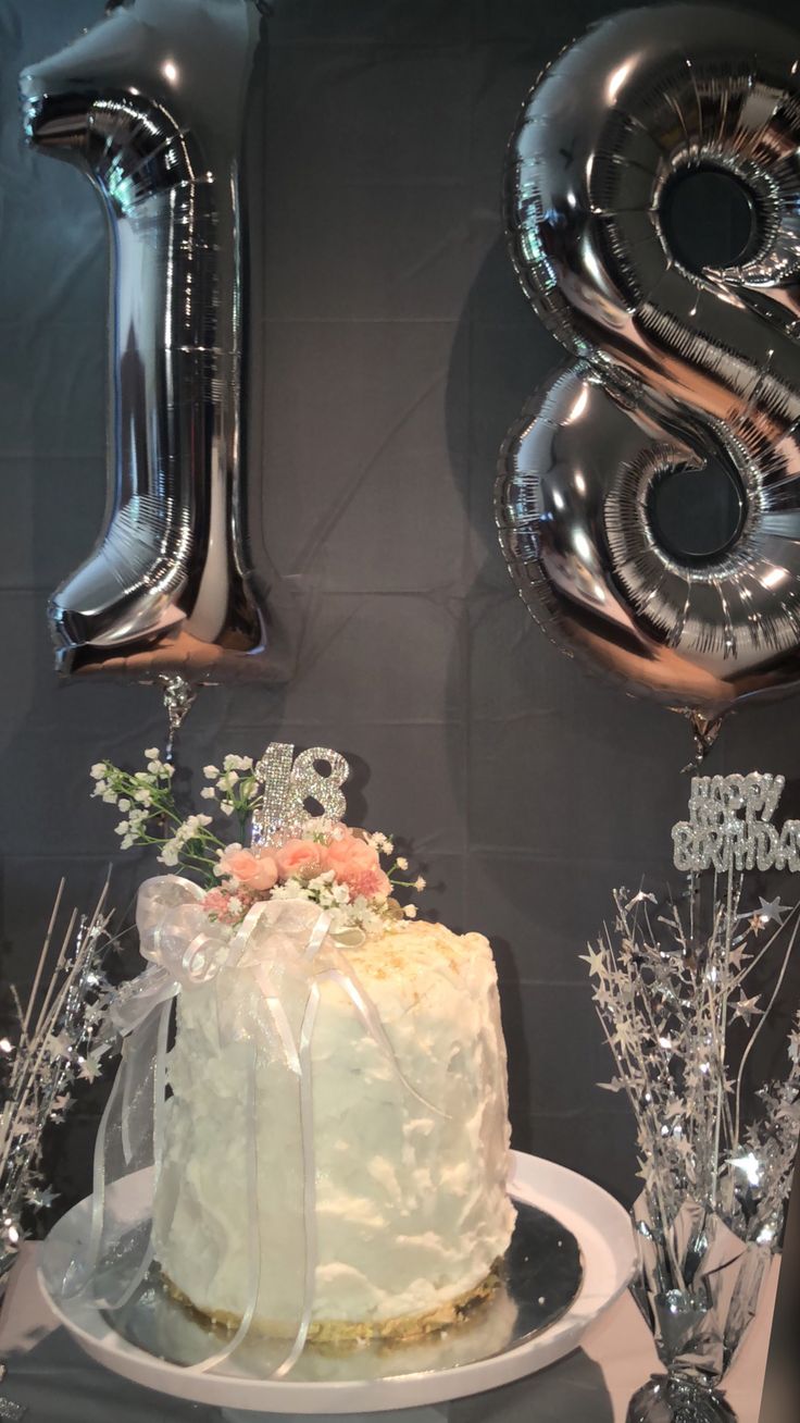 a white cake sitting on top of a table next to balloons and silver numbers that spell out the number twenty