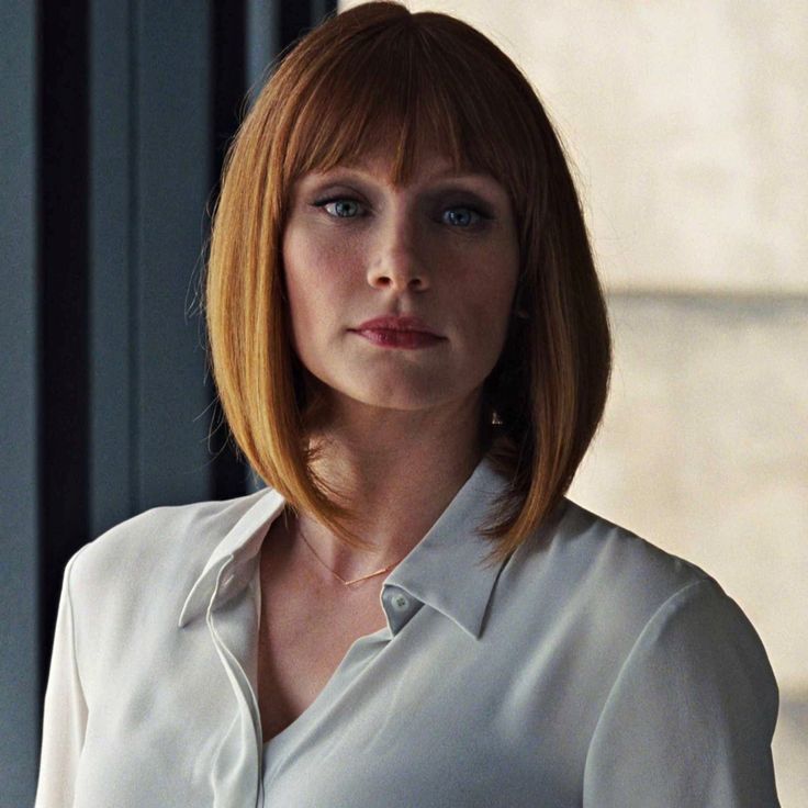 a woman with red hair wearing a white shirt and looking off to the side in front of a window