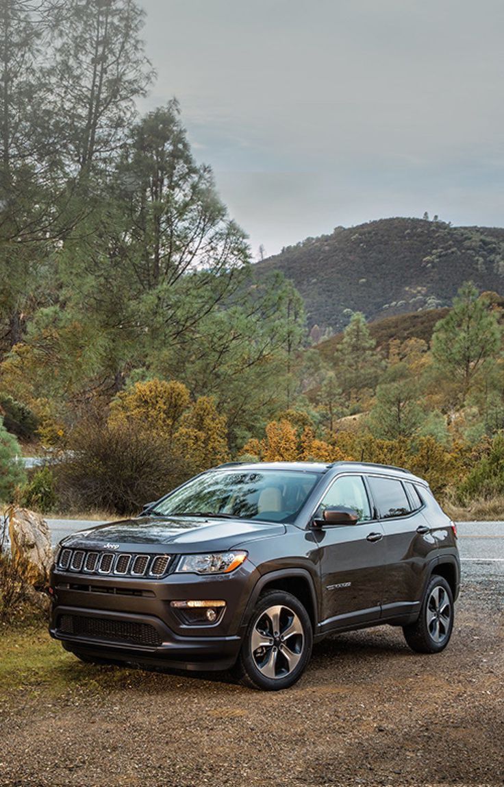 the jeep compass is parked in front of some trees and bushes near a body of water