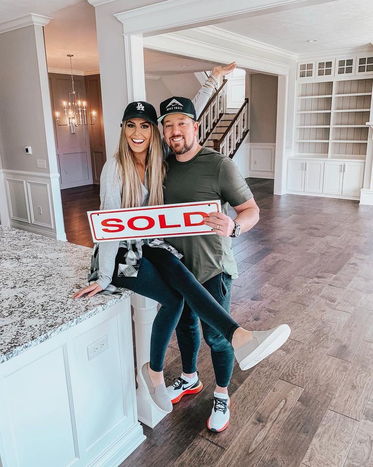 a man and woman holding up a sold sign