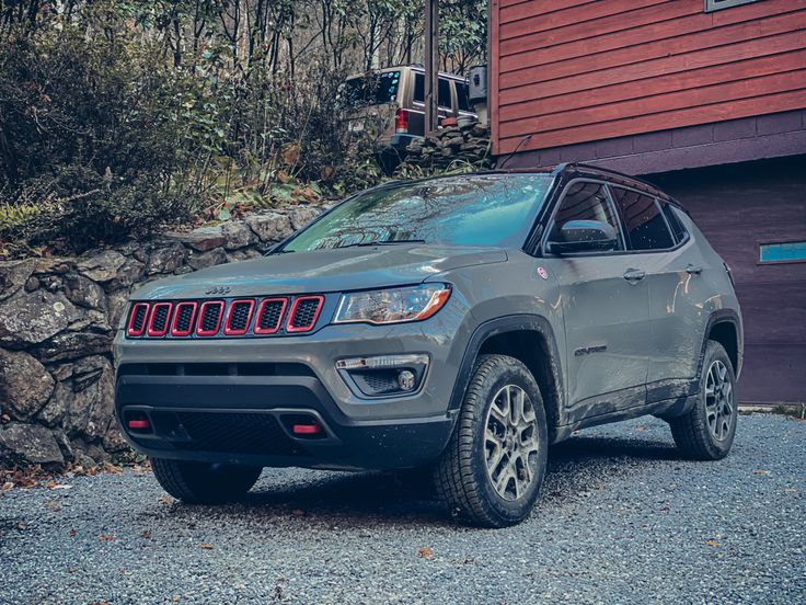 a grey jeep is parked in front of a red house and some rocks on the ground