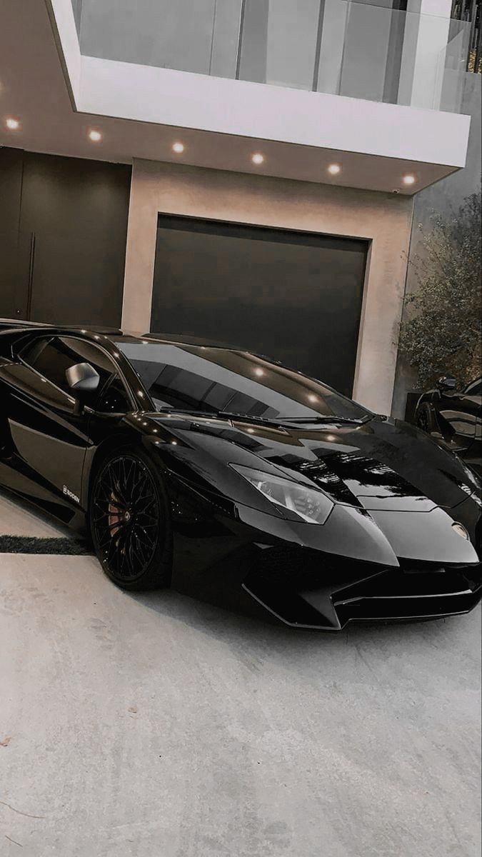 a black sports car parked in front of a modern house with two garage doors open