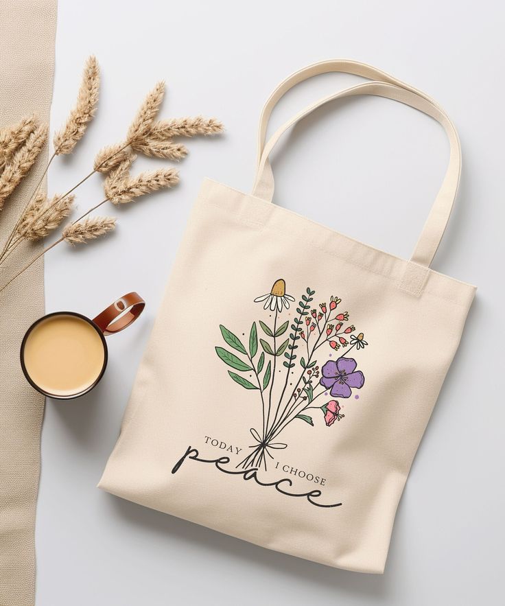 a tote bag next to a cup of coffee and some dried flowers on a table