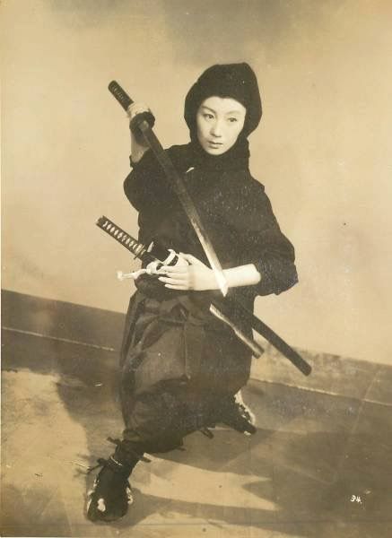 an old black and white photo of a woman holding two swords in one hand and wearing a hat on the other