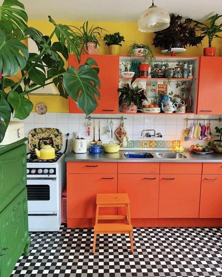 a kitchen with orange cabinets and black and white checkered flooring, potted plants on the wall