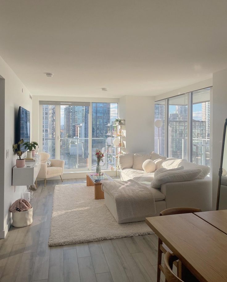 a living room filled with furniture next to tall windows and a wooden table on top of a hard wood floor