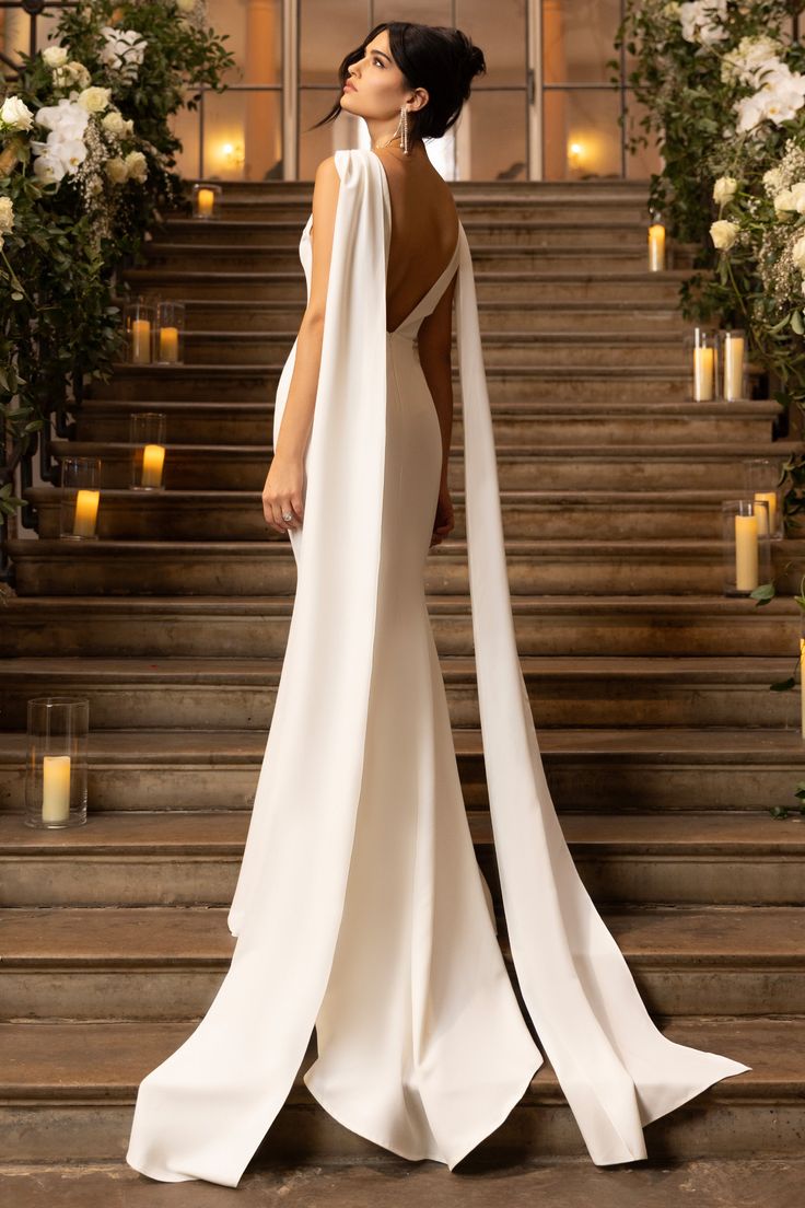 a woman in a white dress standing on some steps with candles and flowers behind her