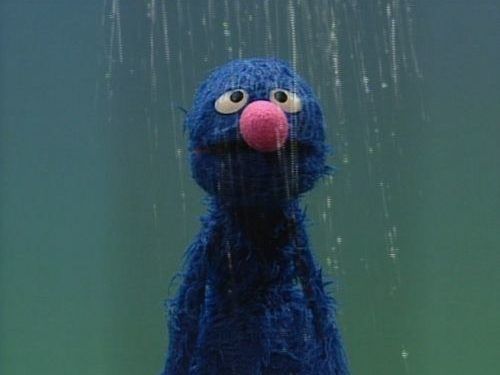 a blue stuffed animal with big eyes and a pink nose standing in front of rain drops