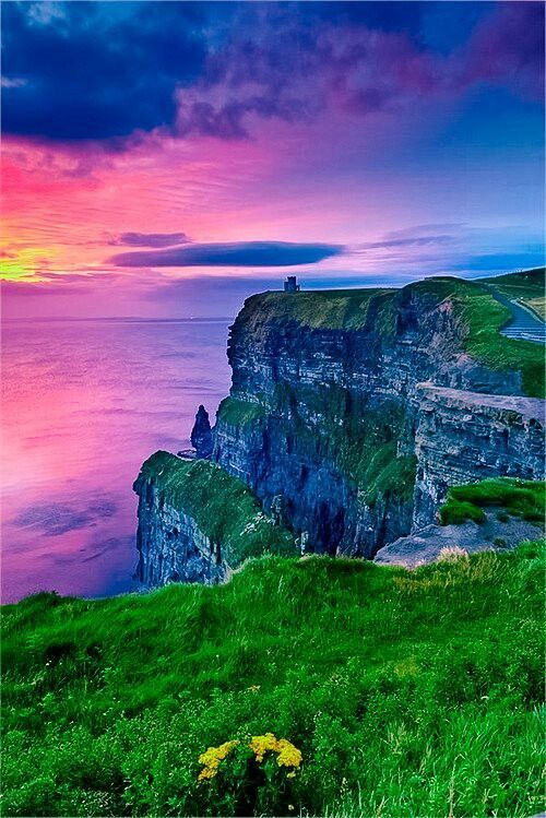 the sun is setting at the edge of an ocean cliff with cliffs in the foreground