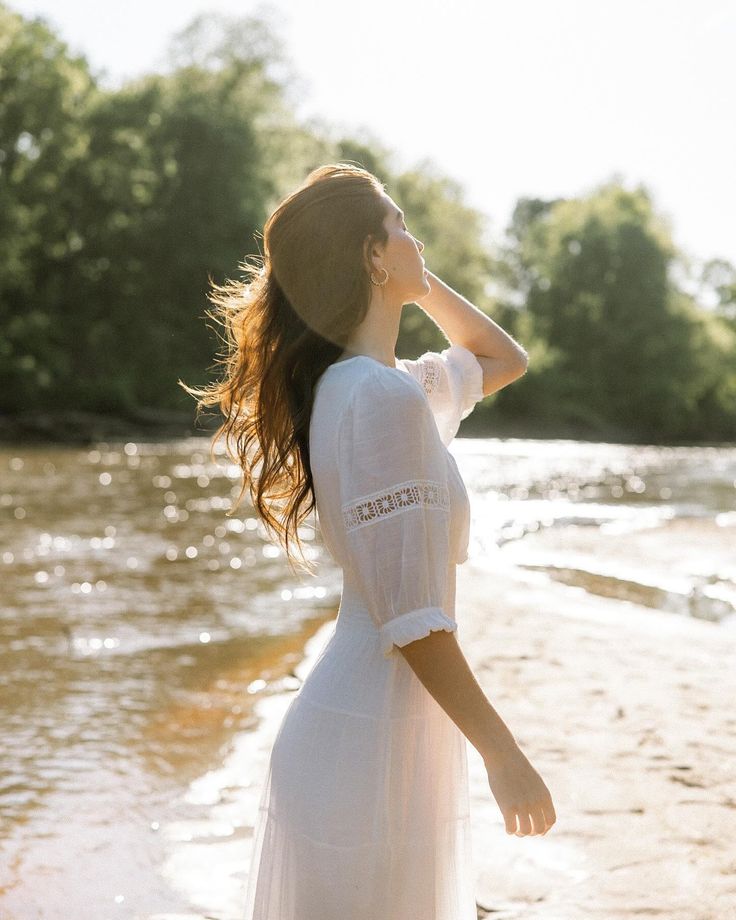 a woman is standing on the beach looking into the distance while wearing a white dress