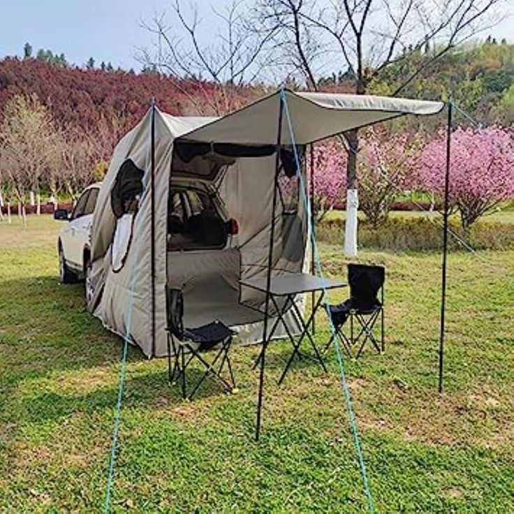 a tent set up in the grass with two chairs and an awning attached to it