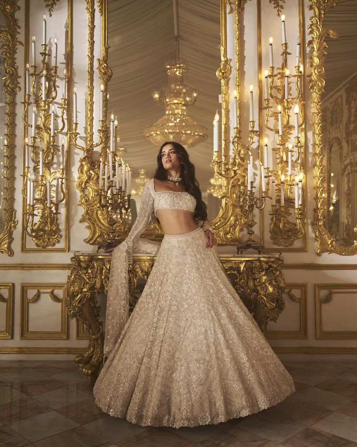 a woman in a white and gold gown standing next to a golden chandelier