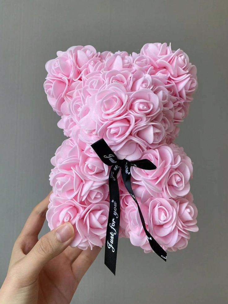 a hand holding a teddy bear made out of pink roses with a black ribbon around its neck