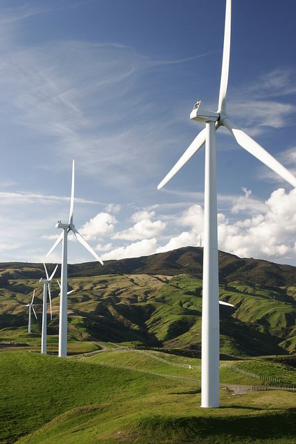 several wind turbines on a grassy hill under a blue sky