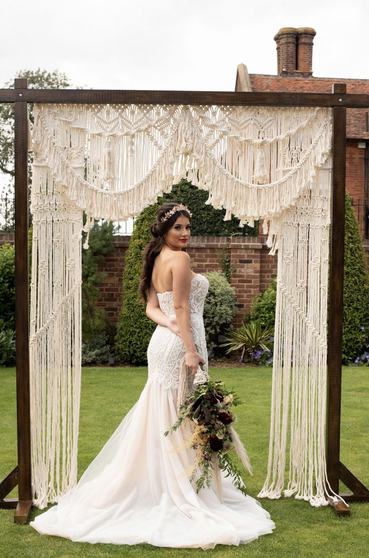 a woman in a wedding dress standing under an arch with macrame hanging from it