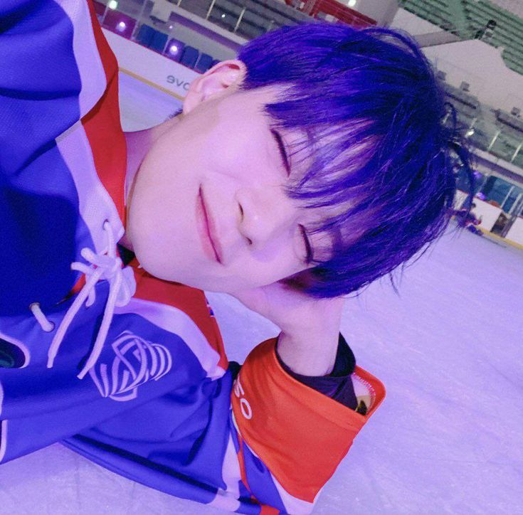 a young man with purple hair laying on an ice rink