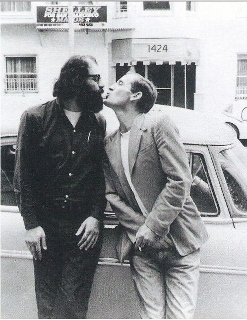 two men standing next to each other in front of a car and one is kissing the other