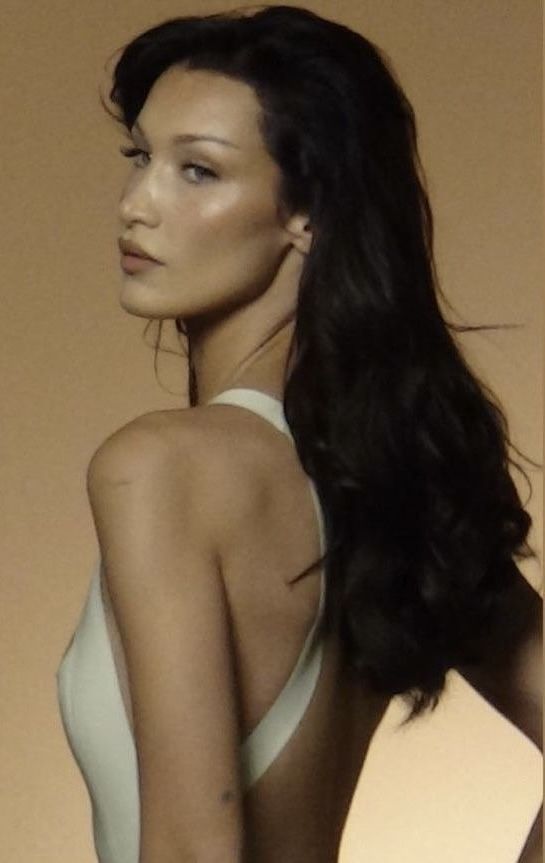 a woman with long black hair standing in front of a wall