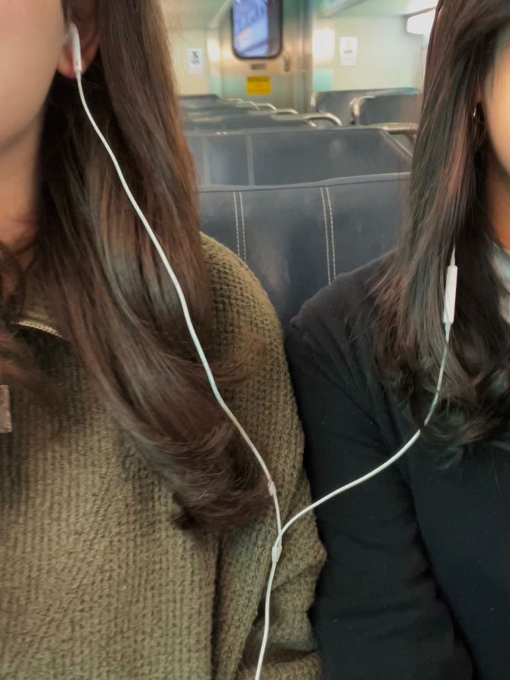 two women sitting on a train with headphones in their ears and one wearing a sweater