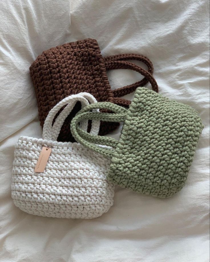 three crocheted purses sitting on top of a white bed next to each other