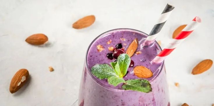 a purple smoothie with fruit and nuts on the side, topped with a striped straw