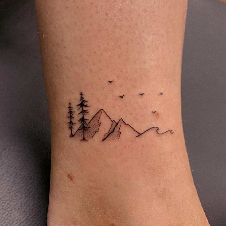 a tattoo on the foot of a person with mountains and birds in the sky behind them
