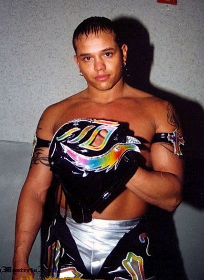a man with tattoos on his arm and chest wearing a black leather outfit, standing in front of a wall