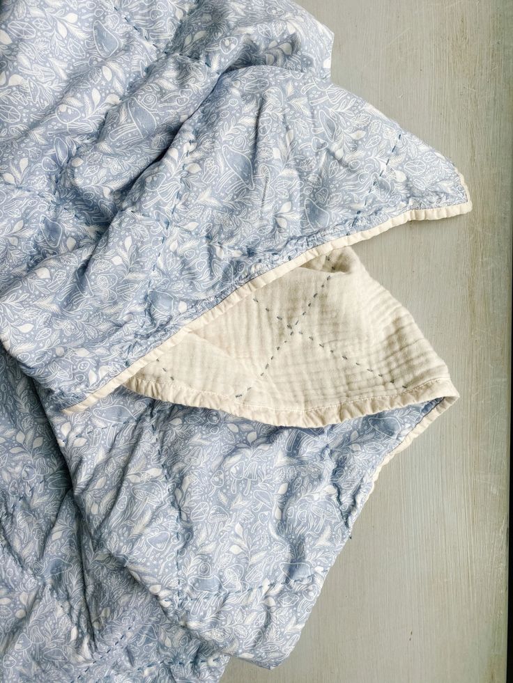 an unmade bed with blue and white comforter on it's side next to a pillow