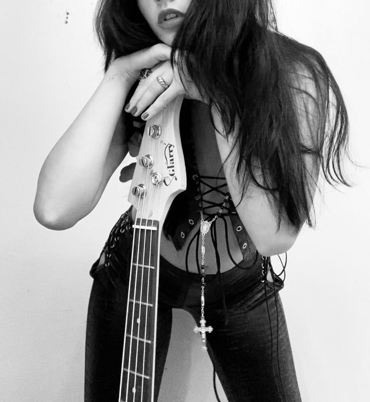 a woman with long hair and piercings is holding a bass in her hands while leaning against a wall