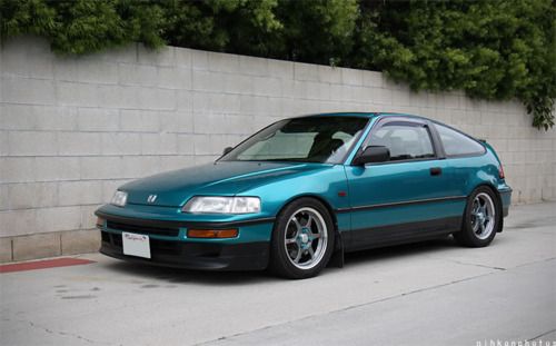 the blue car is parked on the side of the road next to a concrete wall