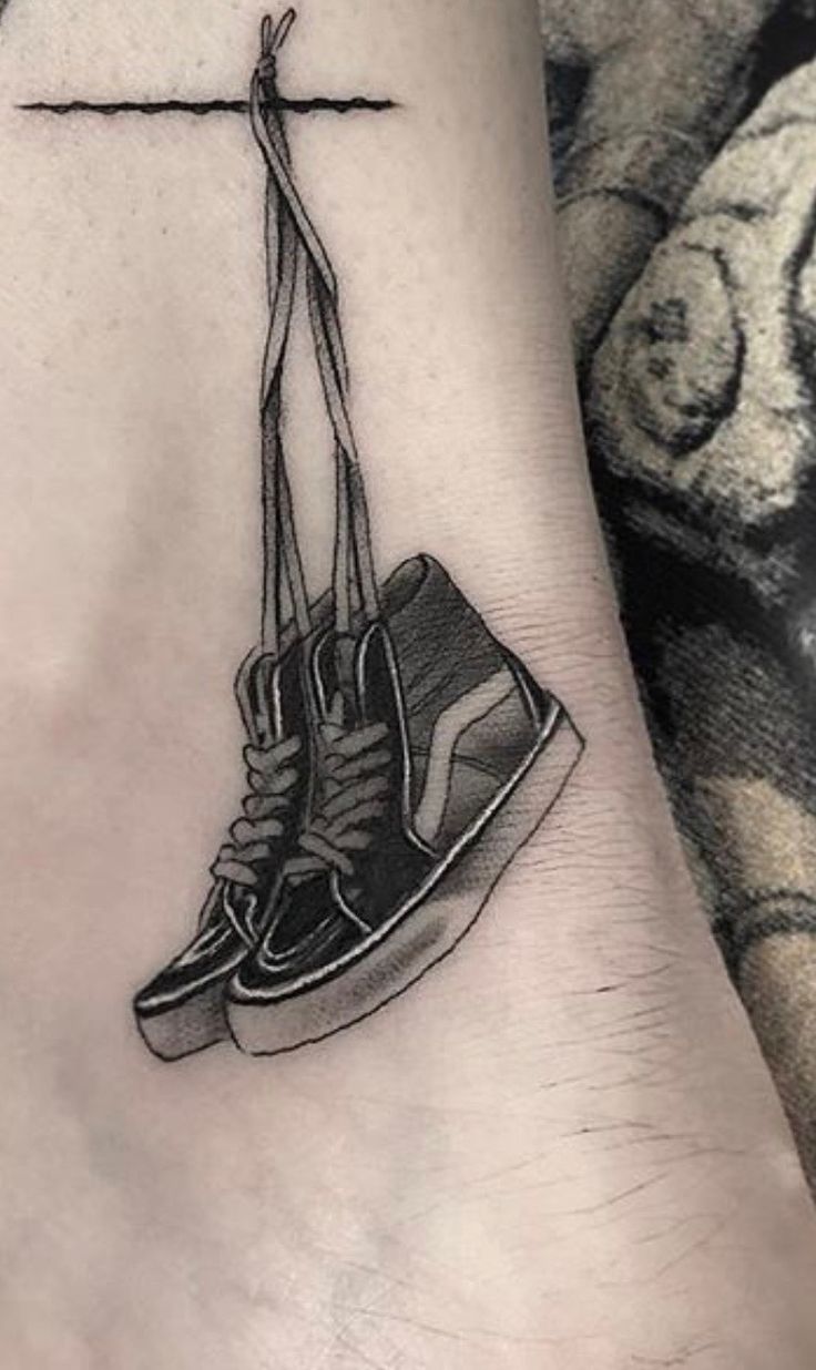 a tattoo on the foot of a person with a pair of shoes hanging from it