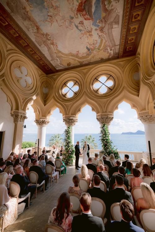 a wedding ceremony in an ornate building overlooking the ocean