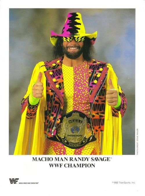 a man in a yellow and pink outfit holding a wrestling belt with his thumbs up