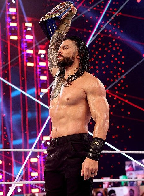 a shirtless man holding up a trophy on top of his head in the middle of a wrestling ring