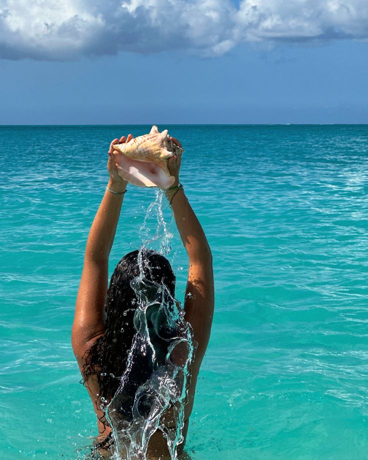 a woman standing in the ocean holding up a shell