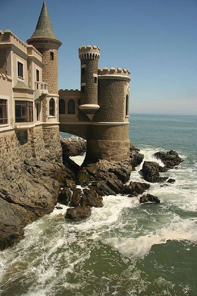 an old castle sitting on top of a rocky cliff next to the ocean with waves crashing in front of it