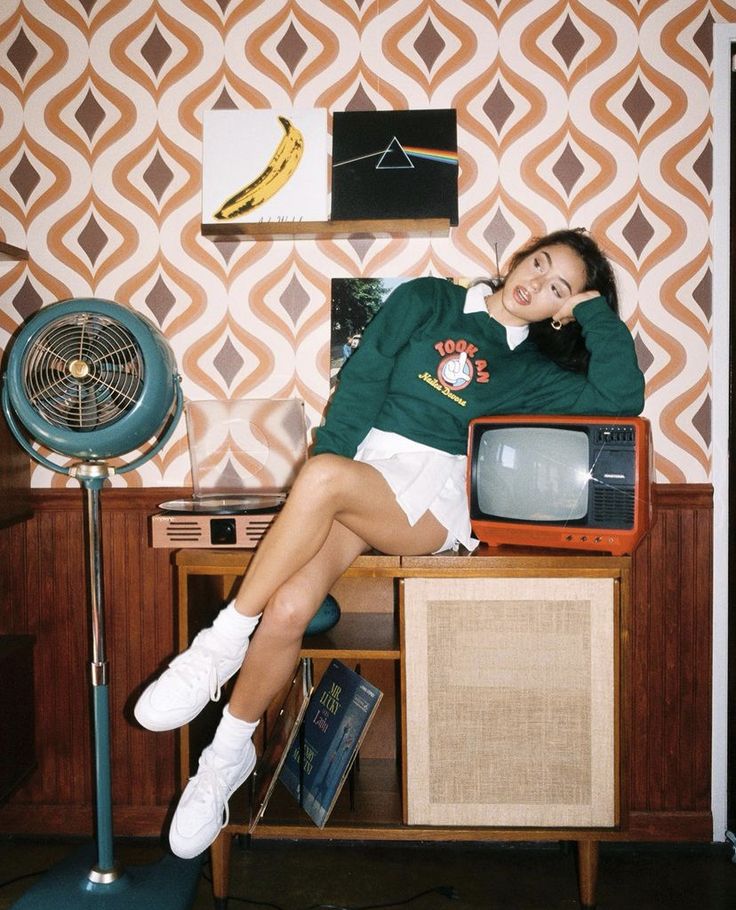 a woman sitting on top of a table next to an old fashioned tv and fan