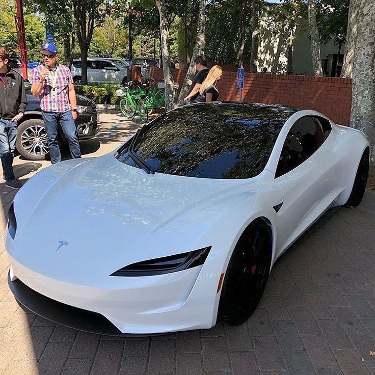 a white car is parked on the side of the road with people walking by it