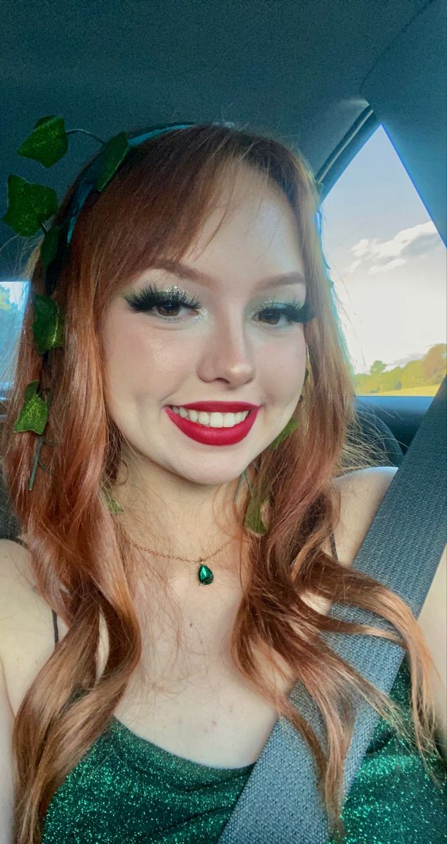 a woman with red hair and green leaves on her head sitting in the back seat of a car