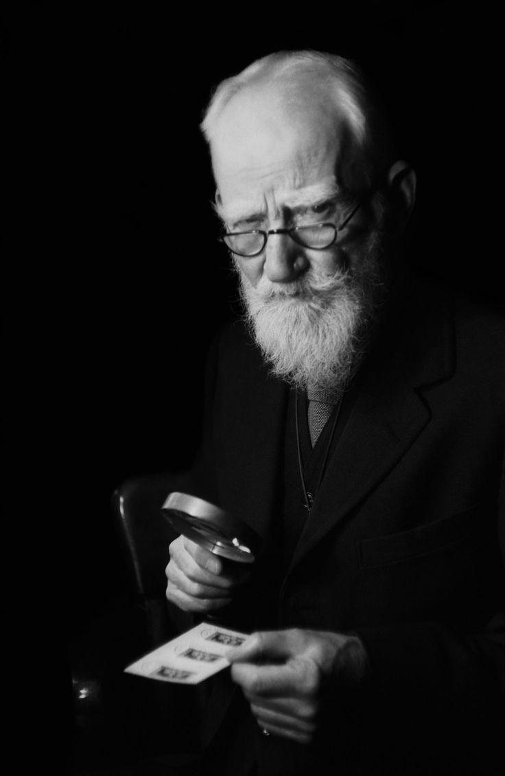 black and white photograph of an old man with glasses reading a book while holding a magnifying glass