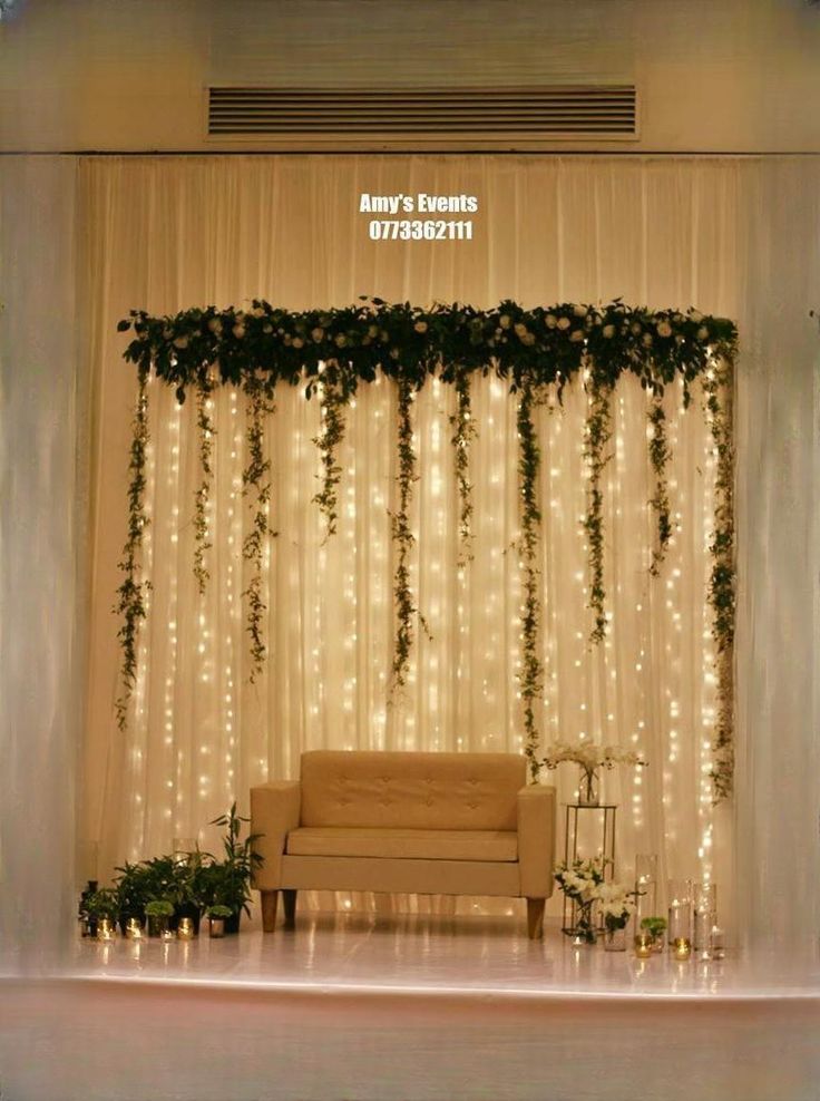 a couch sitting in front of a white curtain covered wall with greenery on it