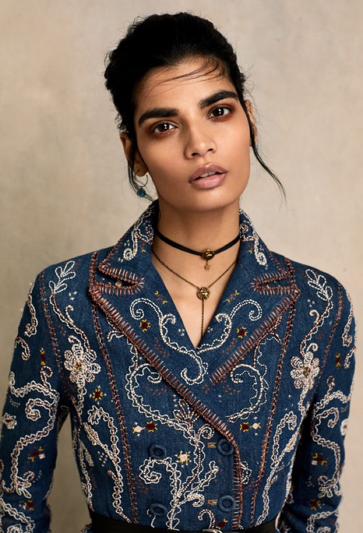 a woman wearing a blue shirt and black skirt with an intricate design on the front