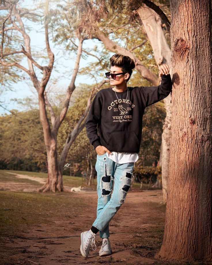 a young man standing next to a tree in the forest wearing sunglasses and a black sweatshirt