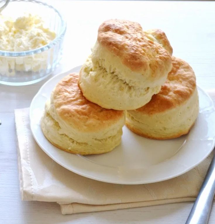 three biscuits on a white plate next to a bowl of cottage cheese and a fork