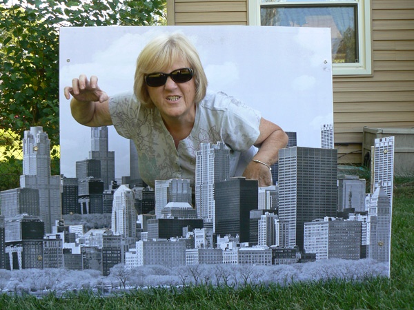 a woman is posing in front of a cutout of a cityscape with sunglasses on
