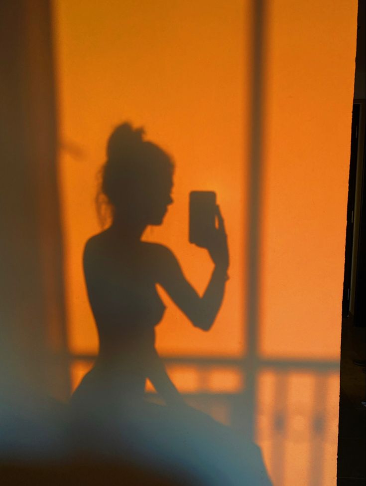 a woman sitting in front of a window taking a photo with her cell phone while holding a camera