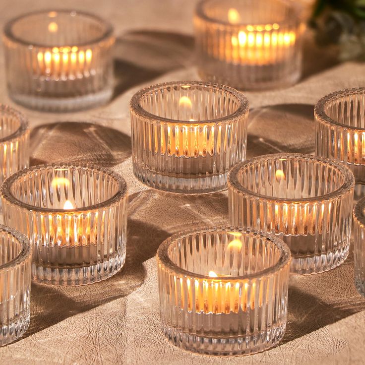 many clear glass candles are lit on the table